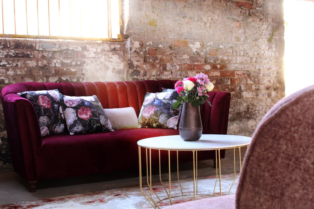 Velvet couch with floral cushions and gold frame table – boutique event furniture