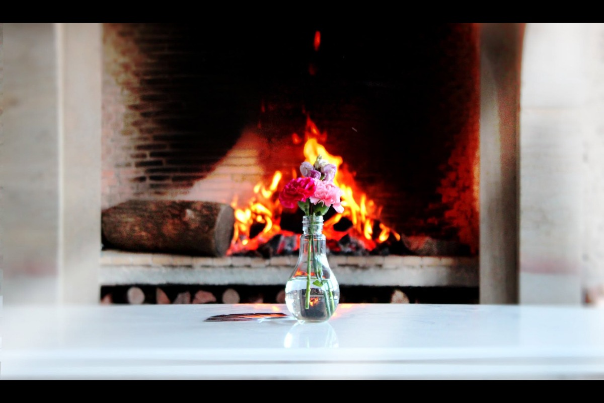 Single vase with flowers in front of a lit fireplace